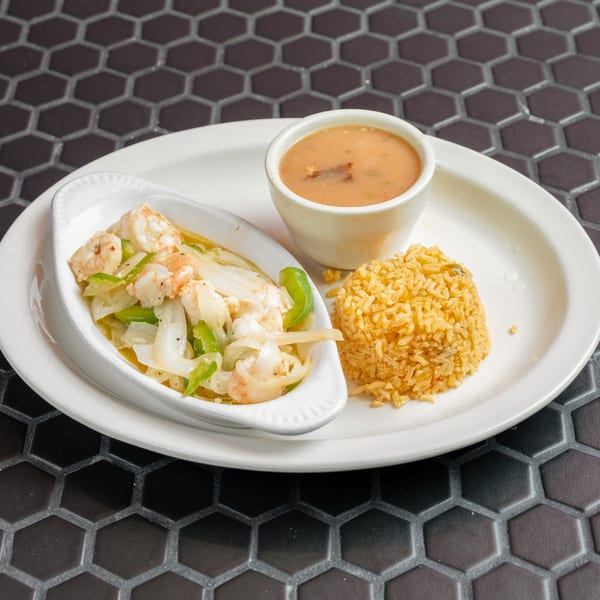 Shrimp with onions and peppers, a side of rice, and a cup of soup on a white plate.