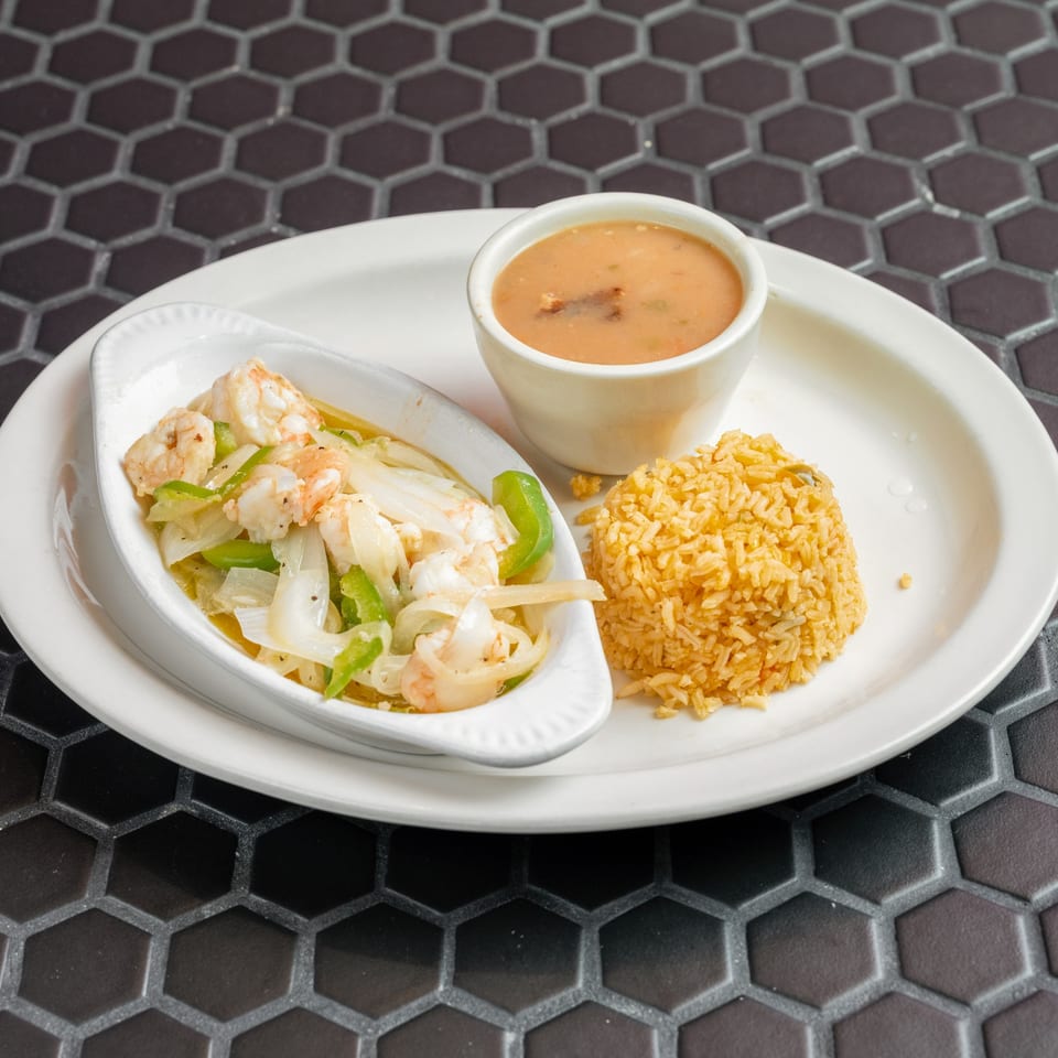 Shrimp with onions and peppers, a side of rice, and a cup of soup on a white plate.