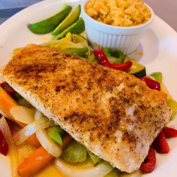 Grilled fish fillet with sautéed vegetables, avocado slices, and a side of rice.
