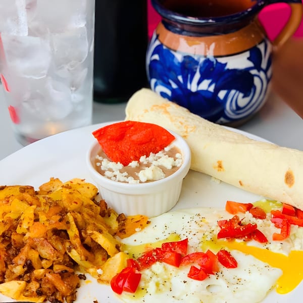 Mexican breakfast with fried eggs, potatoes, beans, tortilla, and a blue and white ceramic mug.