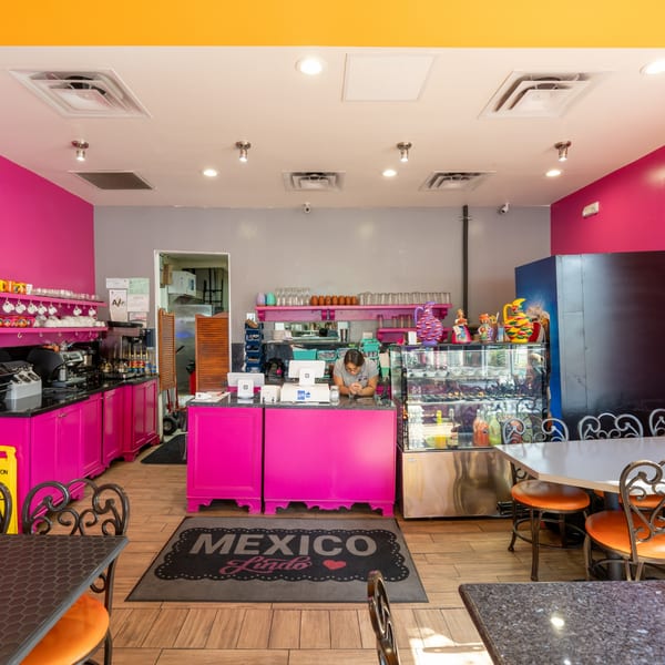 A vibrant Mexico Lindo Restaurant interior with pink counters, a server, and a "Mexico Lindo" mat.