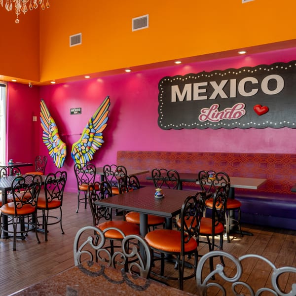 Vibrant Mexico Lindo Restaurant interior with pink walls, orange ceiling, colorful wings art, and black tables with orange chairs.