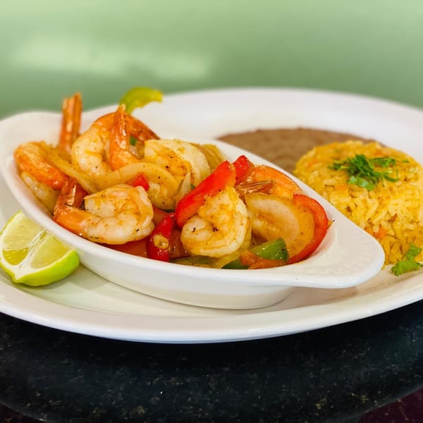 Shrimp fajitas with bell peppers and onions, served with Mexican rice, refried beans, and lime.