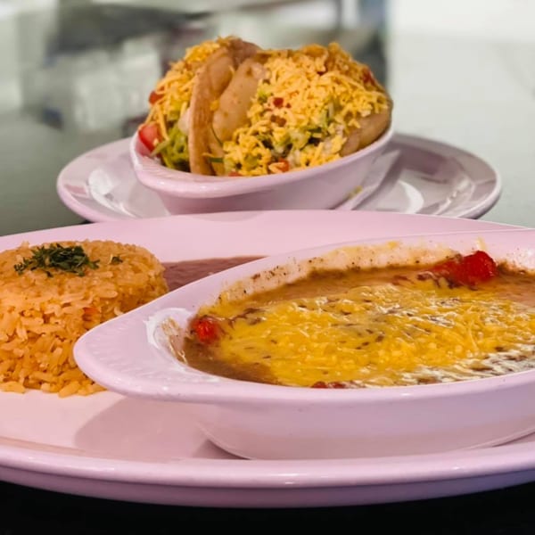 A Mexican meal with tacos, rice, and a cheesy bean dish on white plates.