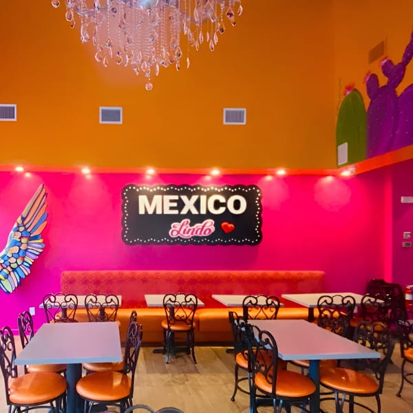 Vibrant Mexico Lindo Restaurant interior with pink and orange walls, a neon sign, and colorful decor.