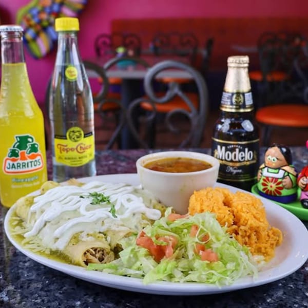 Mexican enchiladas with rice, salad, and a side of soup, with Jarritos and Modelo drinks.