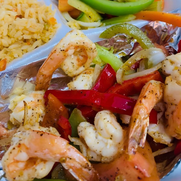 Close-up of Mexican shrimp fajitas with bell peppers, onions, and rice in a foil container.
