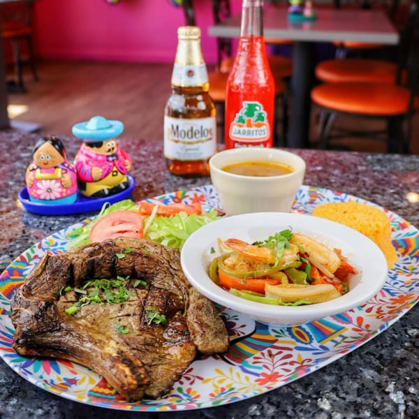 Grilled steak, shrimp fajitas, rice, salad, soup, and drinks on a colorful Mexican plate.